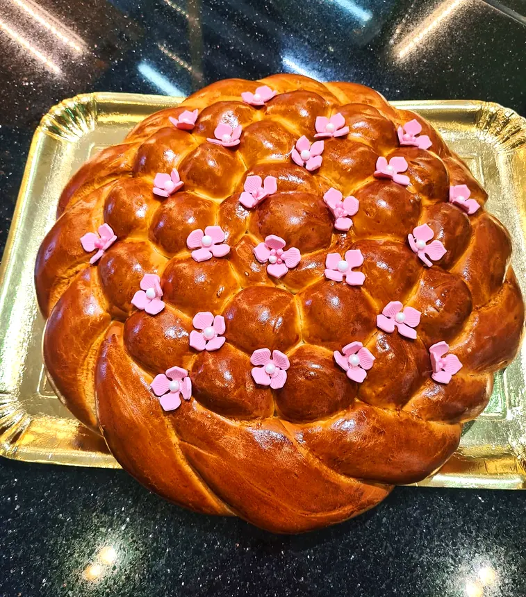 Colac împletit auriu, decorat cu flori roz din fondant, pe tavă aurie